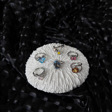 Overview of the Future Spark ring collection, showcasing a variety of distinctive silver-toned rings with vibrant gemstones, presented on white stands with a contrasting dark, moody backdrop.