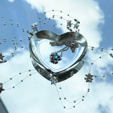 Future Spark Seren star necklace creating a dreamy brand atmosphere, displayed in a reflective heart dish mirroring the sky, with surrounding star bead accents.
